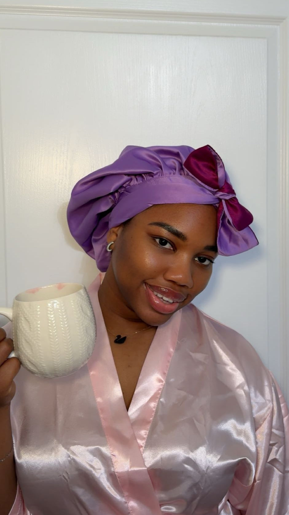 Woman in a pink satin robe holding a white mug with out satin tie bonnets 